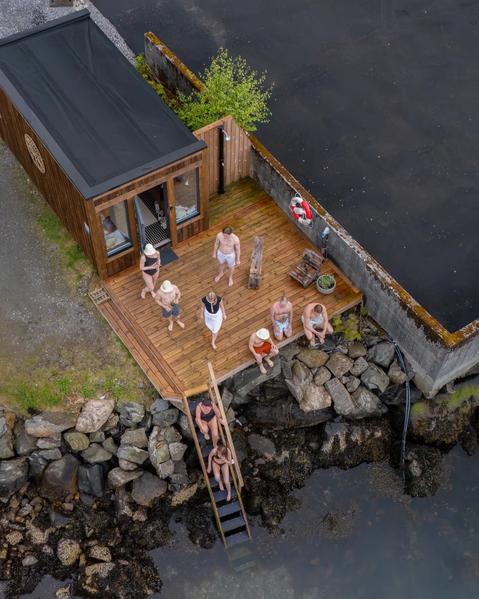 Ni badegjester på bryggen ved Kjøkkelvik Sauna, sett ovenfra, to av dem på vei ned stigen i sjøen