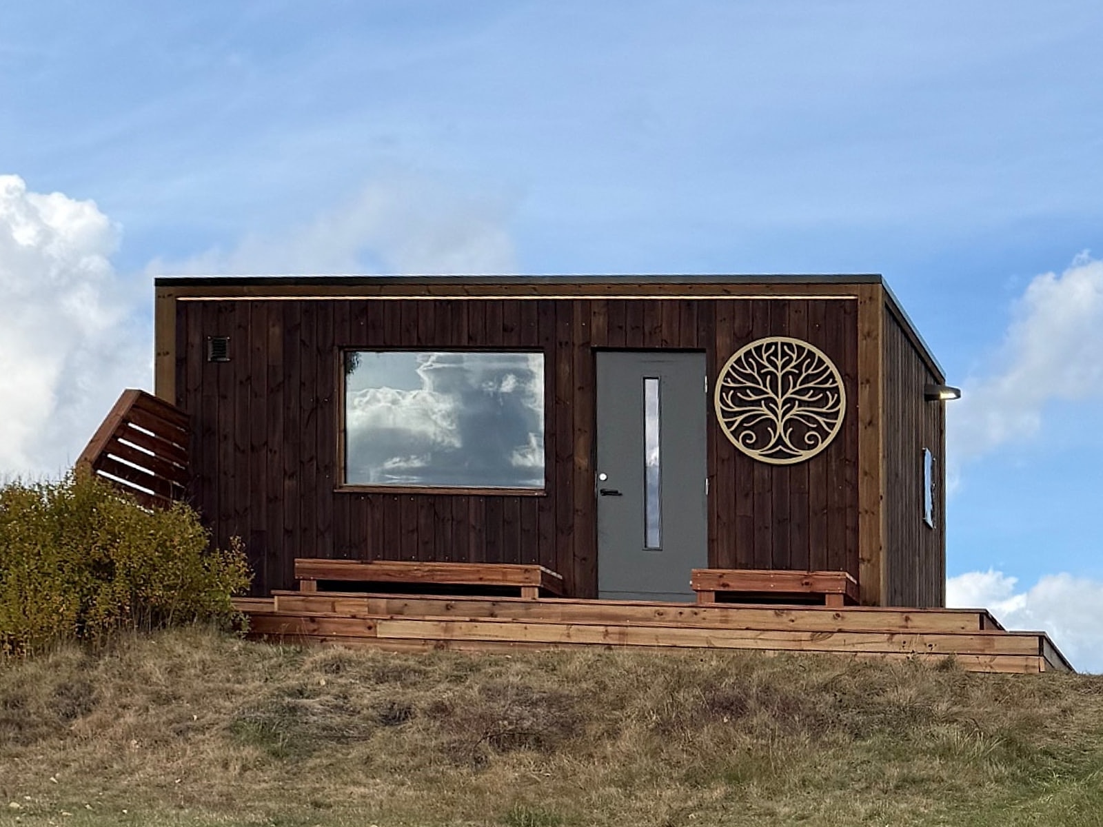 Storenga Sauna sett forfra: mørk trekledning, stort vindu, inngangsdør og terrasse med benker